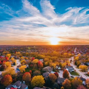 Aerial view of a Kansas City neighborhood at sunset in the fall, with colorful autumn trees and houses under a vibrant sky.