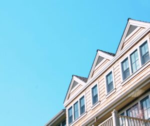 Exterior view of a house with multiple dormer windows and beige siding against a blue sky.