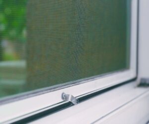Close-up of a window screen mesh with latch on a white window frame.