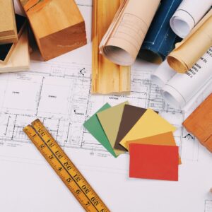 Home renovation planning tools including wood samples, color swatches, blueprints, and a measuring ruler spread across a table.
