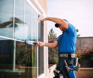 Professional window cleaner in blue uniform washing a large sliding glass window outside.