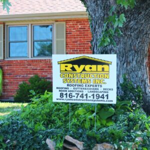 Ryan Construction Systems Inc. yard sign in front of a brick home, advertising roofing, gutters, decks, room additions, and landscaping services in Kansas City.