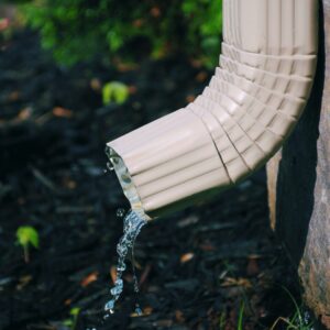 Water flowing from a clean downspout onto mulch, illustrating proper gutter drainage and fall roof maintenance for Midwest homes.