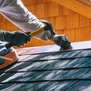 Roofer installing metal flashing along roof edge with a hammer, demonstrating fall maintenance to prevent winter leaks and ice dam damage in Kansas City.