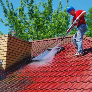 Roofing contractor pressure washing debris off red tile roof near skylight, demonstrating seasonal roof cleaning and fall maintenance preparation in Kansas City.