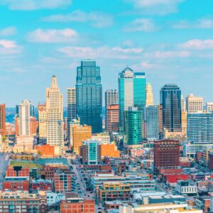 Downtown Kansas City skyline on a bright day, showcasing iconic skyscrapers and urban architecture with blue skies overhead.