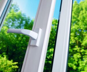 Close-up of a modern white window handle on an open window with green trees outside.