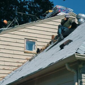 Workers repairing an old shingle roof on a Kansas City home, with shingles and tools stacked nearby for installation.