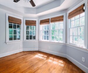 Bright room with bay windows, bamboo blinds, and sunlight reflecting on hardwood floors.